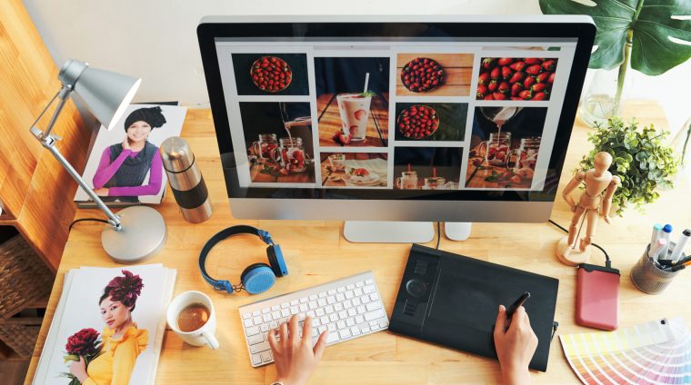 Directly above view of unrecognizable designer choosing photos for magazine page on modern computer in office