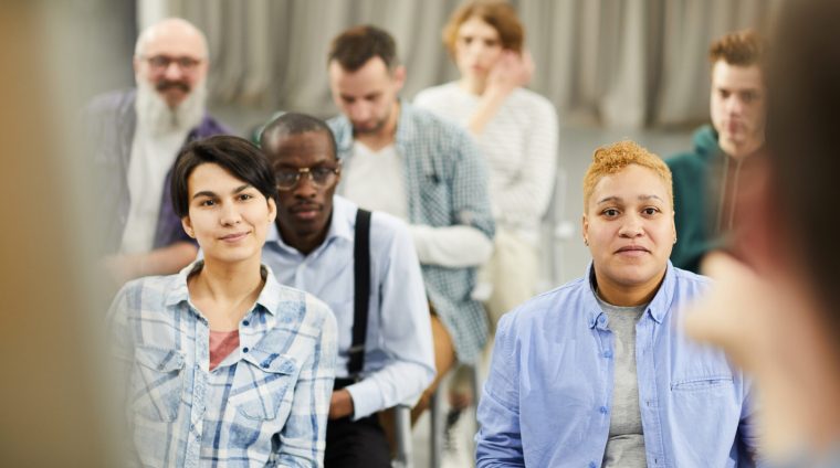 Group of content curious people in casual clothing sitting on chairs and listening to speaker during conference