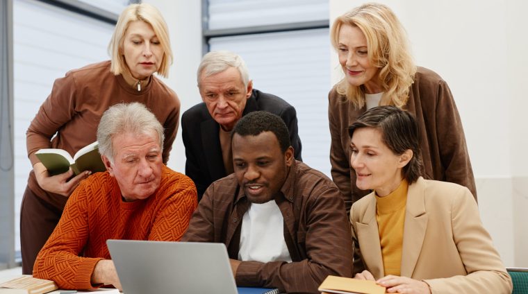 African teacher showing his senior students how to use laptop while they sitting together at desk in classroom